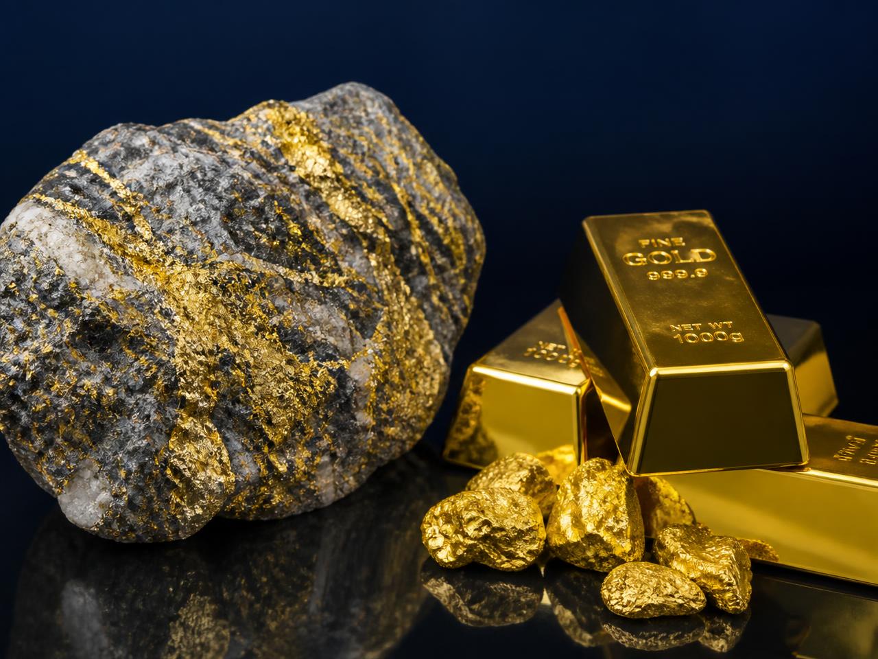 Gold ore specimen beside refined gold bars and nuggets